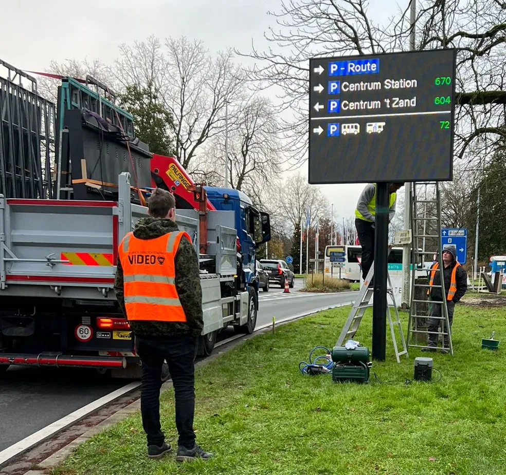 Équipe installant un panneau LED directionnel sur un mât, avec un camion en arrière-plan