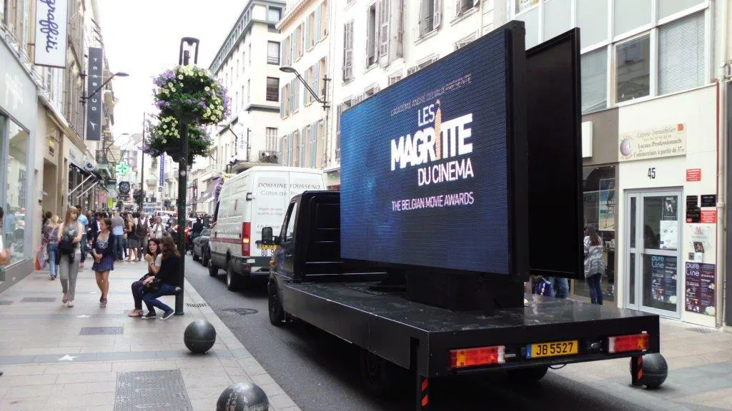 Camion publicitaire équipé d'un écran LED affichant une annonce pour Les Magritte du Cinéma dans une rue animée en milieu urbain